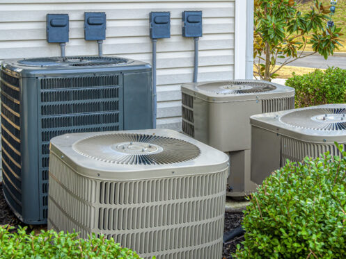 Four Air conditioning units outside an apartment complex.